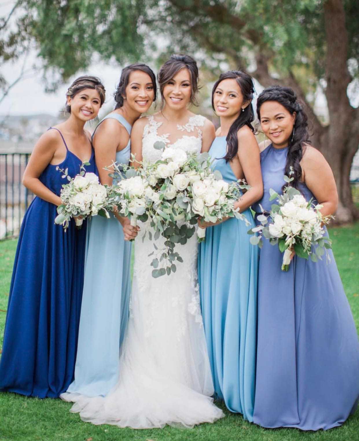 Bridesmaids in blue with bride holding white bouquets, posing outdoors.