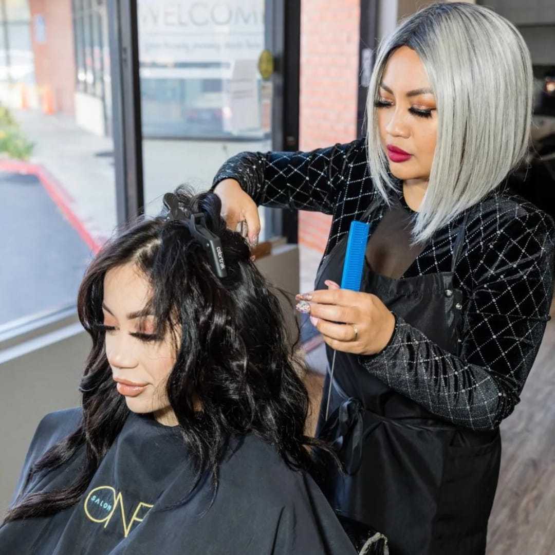 Hair stylist curling client's hair in salon with large windows in the background.