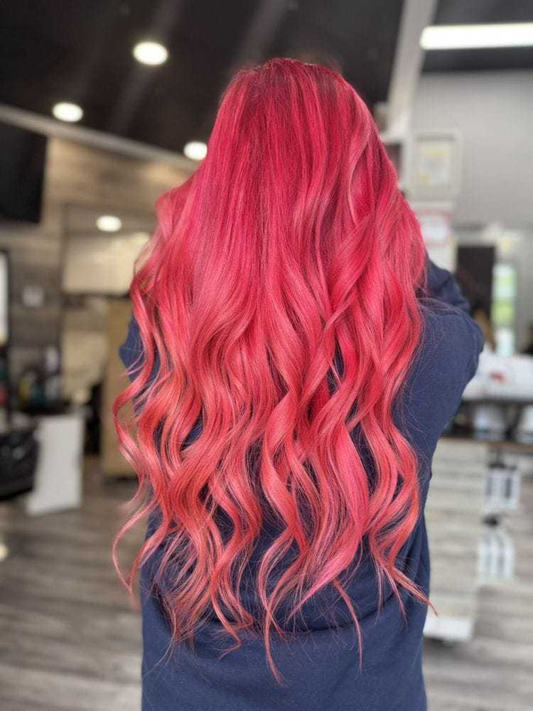 Long vibrant pink wavy hair cascading down a person's back in a salon setting.