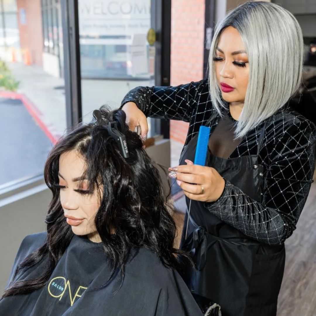 Hair stylist curling client's hair in salon with large windows in the background.