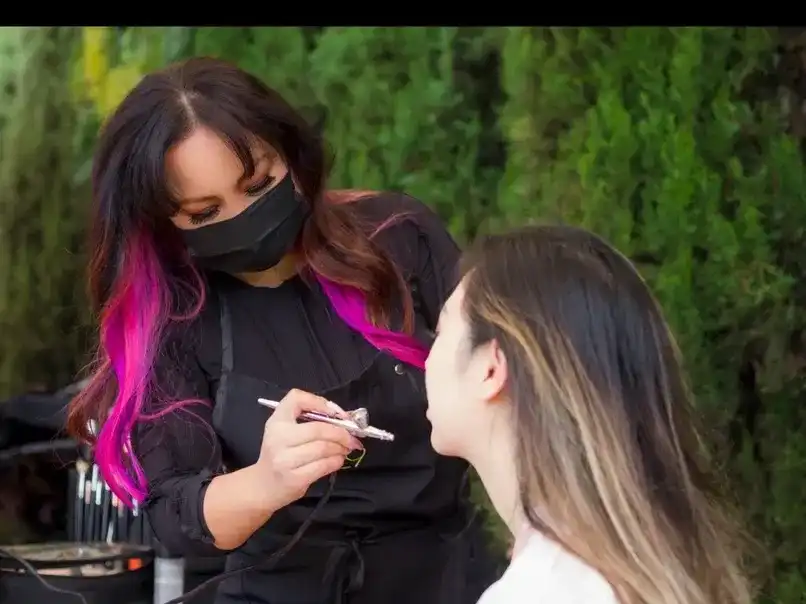 Makeup artist applying foundation with airbrush outdoors.